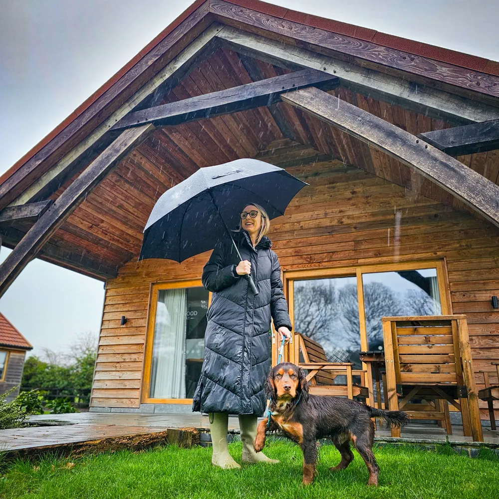 Guest enjoying a rainy day outside a pet-friendly lodge at Hay’s Wood Retreat in Norfolk, accompanied by her dog. Perfect for dog-friendly holidays with comfortable, luxury woodland accommodation.