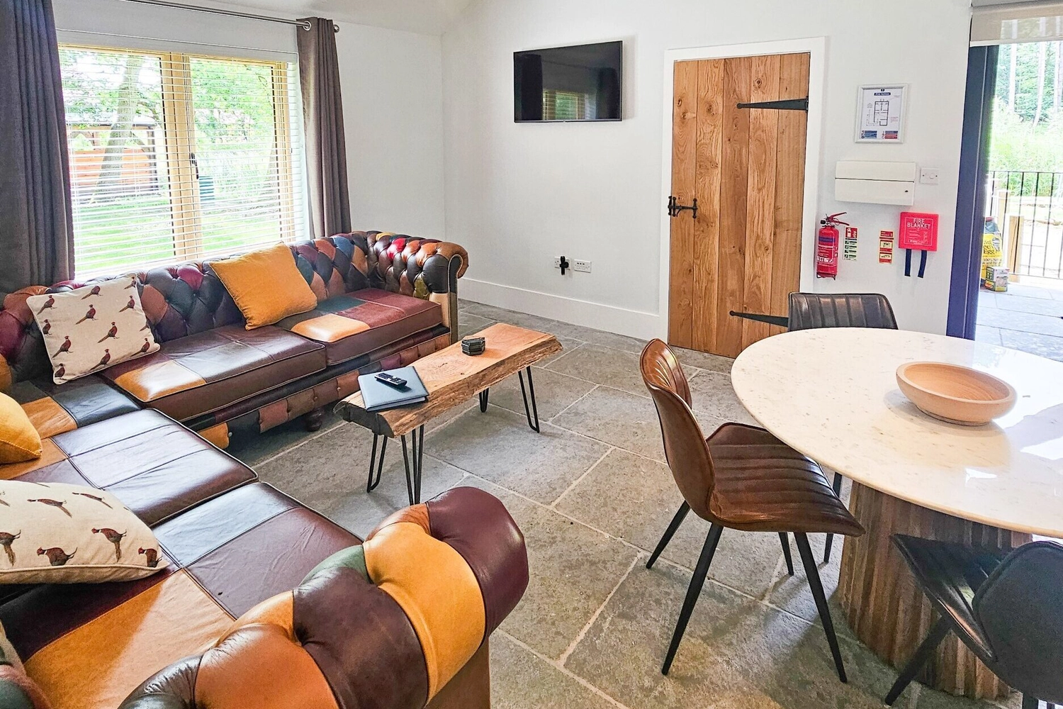 Bright and welcoming living room inside a hot tub lodge at Hay’s Wood Retreat in Norfolk, UK, featuring two comfortable sofas arranged for conversation and relaxation. The open-plan space includes large windows that let in natural light and views of the surrounding woodland, creating a cosy atmosphere for guests enjoying self-catering countryside breaks with family or friends.