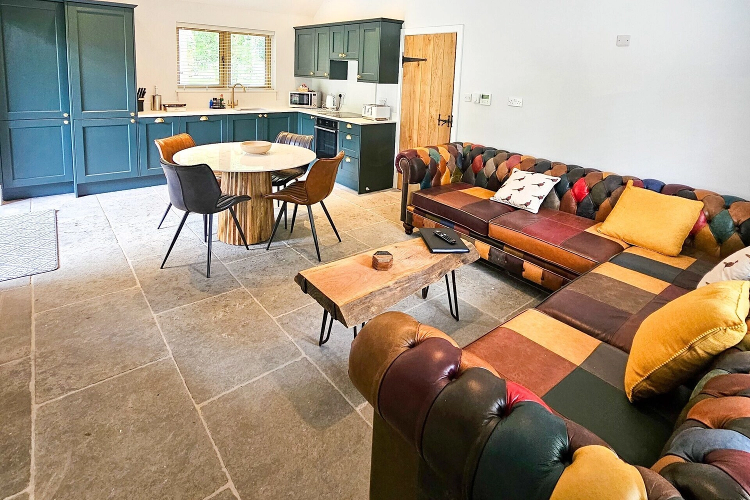 Spacious open-plan living area of a hot tub lodge at Hay’s Wood Retreat in Norfolk, UK, featuring a comfortable sofa, a dining table, and a cosy bedroom area. The room combines rustic charm with modern comforts, offering guests a relaxing self-catering retreat surrounded by peaceful woodland and countryside views, complete with private hot tub access.