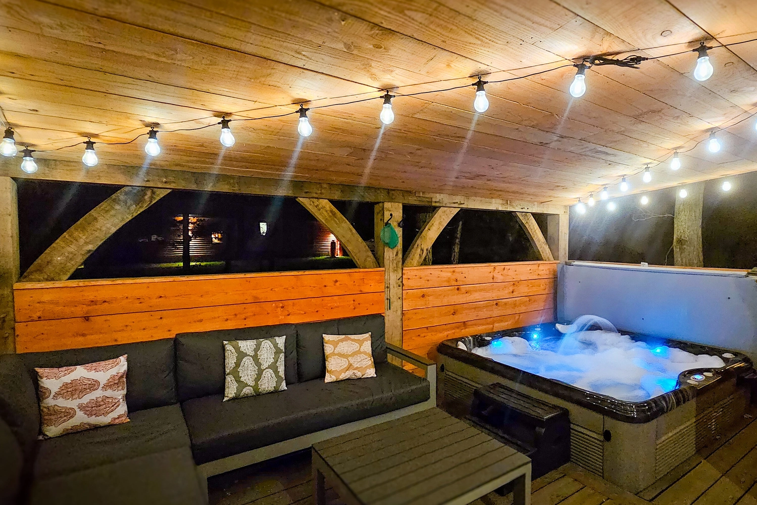 Inviting nighttime view of a hot tub lodge patio at Hay’s Wood Retreat in Norfolk, UK, featuring a bubbling hot tub under a covered patio with warm ceiling lights glowing softly. This luxurious outdoor space offers guests the perfect setting for relaxing evenings, romantic escapes, and countryside hot tub breaks. Hay’s Wood’s hot tub lodges are a popular choice for those seeking peaceful self-catering accommodation with added comfort and ambience in Norfolk.